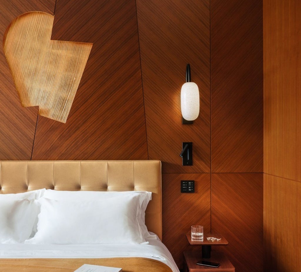 Elegant hotel room with garden views featuring herringbone wood floors, luxe cream furnishings, and custom brass light fixtures