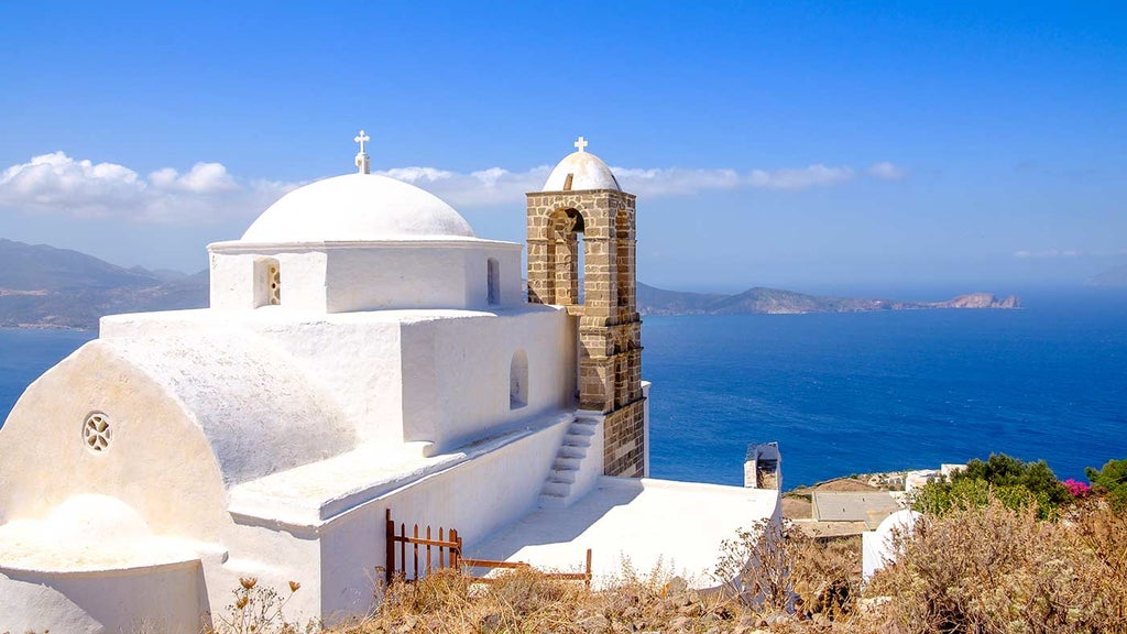 Luxurious white infinity pool overlooking Aegean Sea at sunset, with curved loungers and minimalist Greek architecture in Santorini