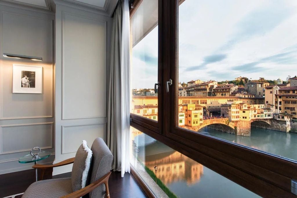 Elegant riverside suite at Portrait Firenze hotel featuring floor-to-ceiling windows, designer furnishings and views of Ponte Vecchio bridge