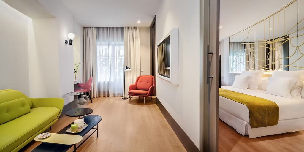 Spacious family suite with modern design, large windows overlooking Madrid, elegant contemporary furnishings, and plush king-sized bed in warm neutral tones