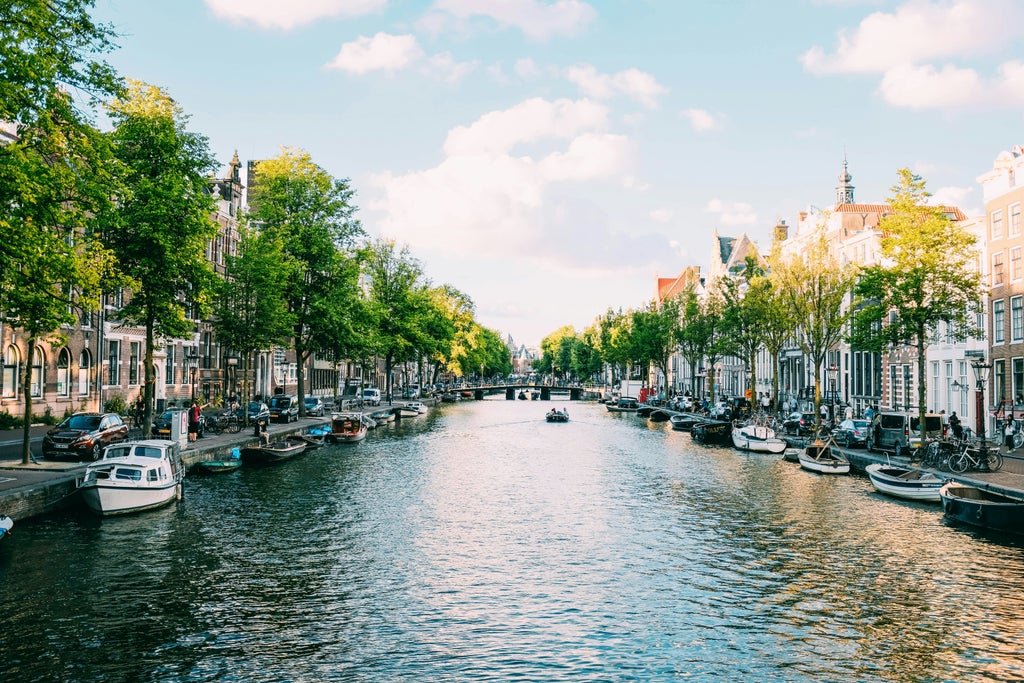 Elegant canal-side townhouses with historic Dutch architecture line Amsterdam's waterway at sunset, reflecting golden light on calm water