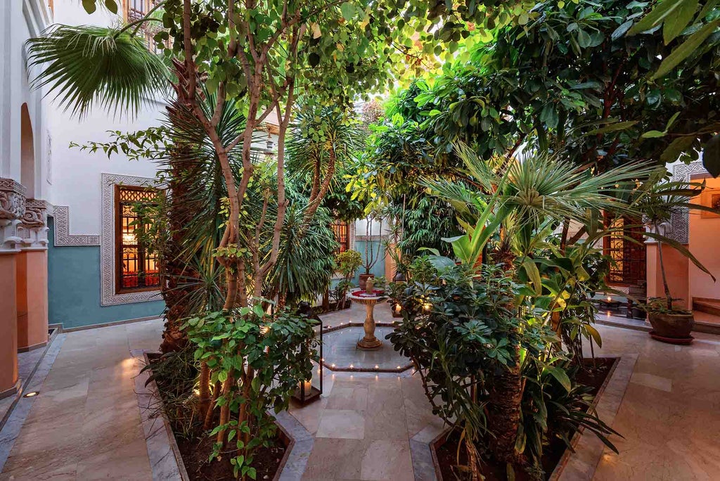 Traditional Moroccan riad courtyard with ornate archways, mosaic tiles, and central fountain, surrounded by potted plants and elegant seating