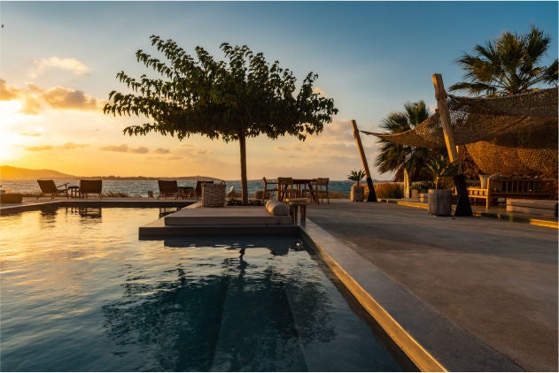 Whitewashed luxury hotel with infinity pool overlooking the Aegean Sea, framed by traditional Greek architecture at sunset