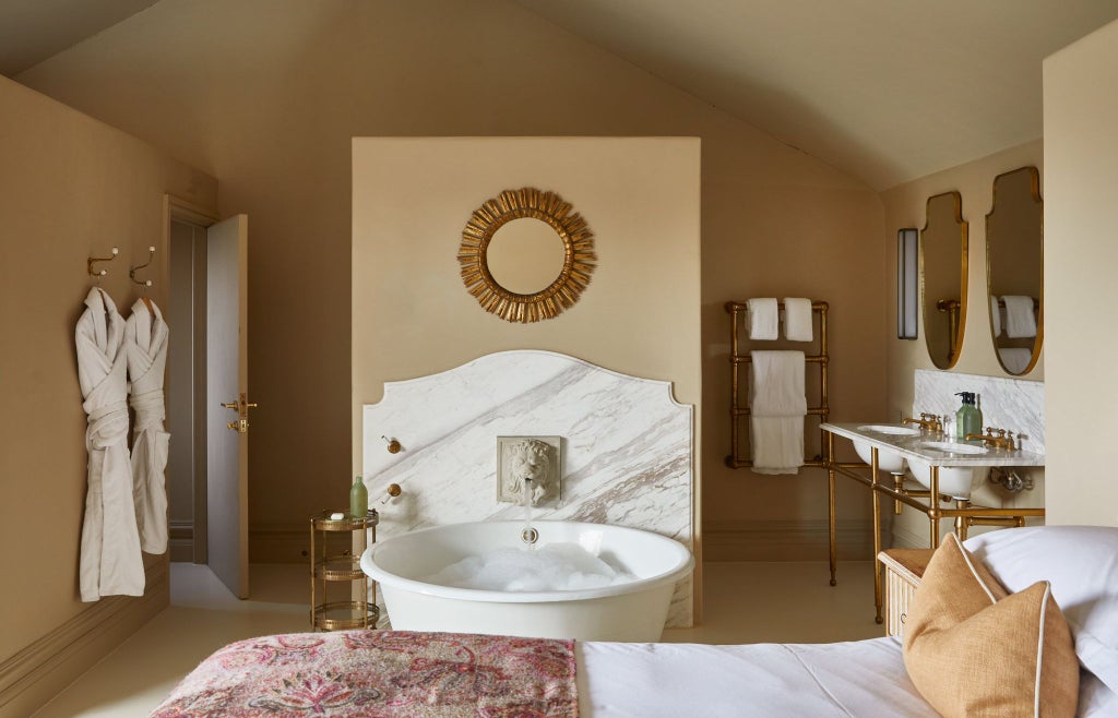 Elegant garden-view bedroom with soft sage linens, plush white bedding, rustic wooden furniture, and soft natural light streaming through sheer curtains