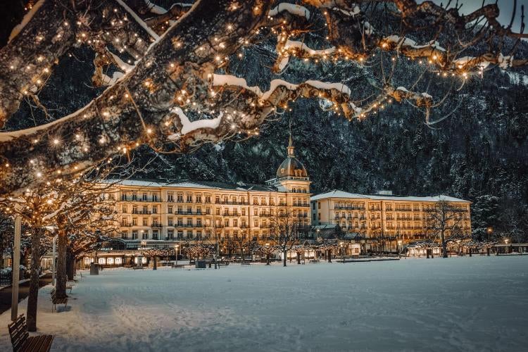 Majestic mountain-view luxury hotel with Belle Époque architecture, ornate facade, and grand balconies overlooking snow-capped Swiss Alps