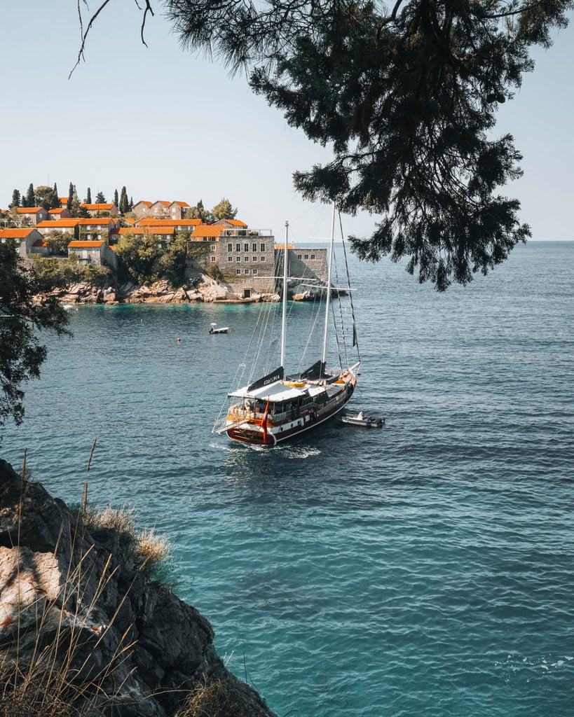 Scenic view of luxury resort in Montenegro Bay with stone buildings nestled into hillside, overlooking turquoise Adriatic waters