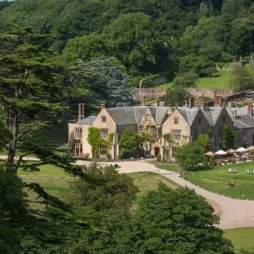 Rustic-chic coastal hotel nestled in Cornwall, with stone walls, sea-view terrace, and lush green landscape blending seamlessly with the rugged scenset countryside