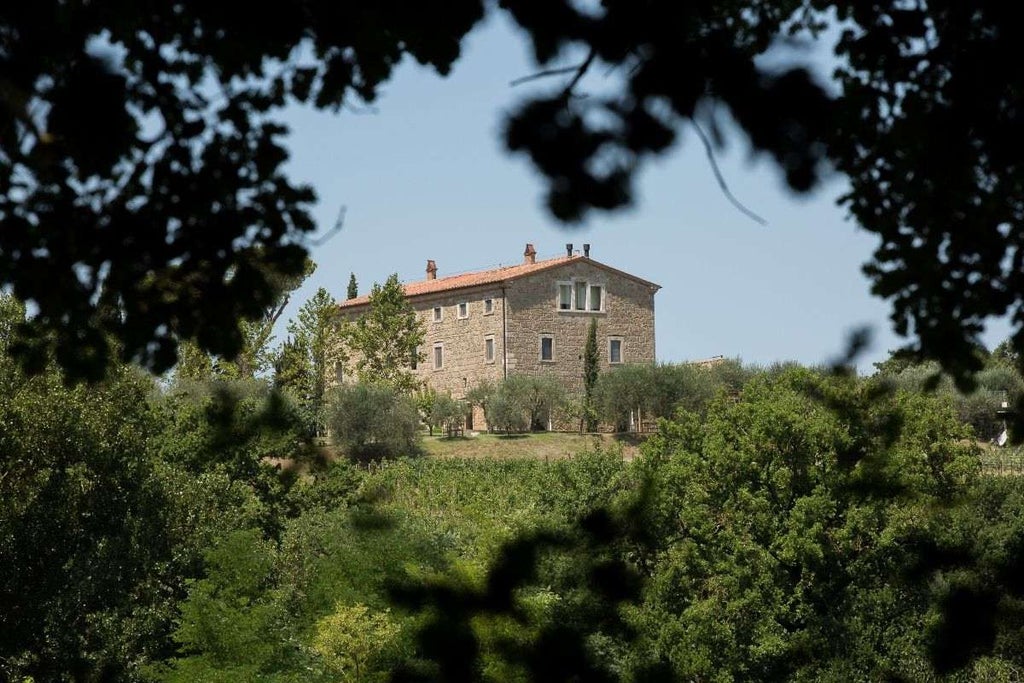 Elegant stone villa with covered terrace overlooking Italian countryside, featuring manicured gardens and sunlit swimming pool