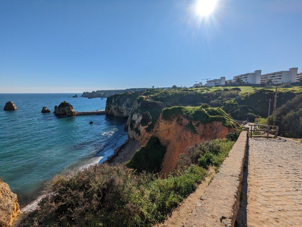 Hikers traverse scenic clifftop trails along the Algarve coastline at sunset, with dramatic rock formations and turquoise waters below