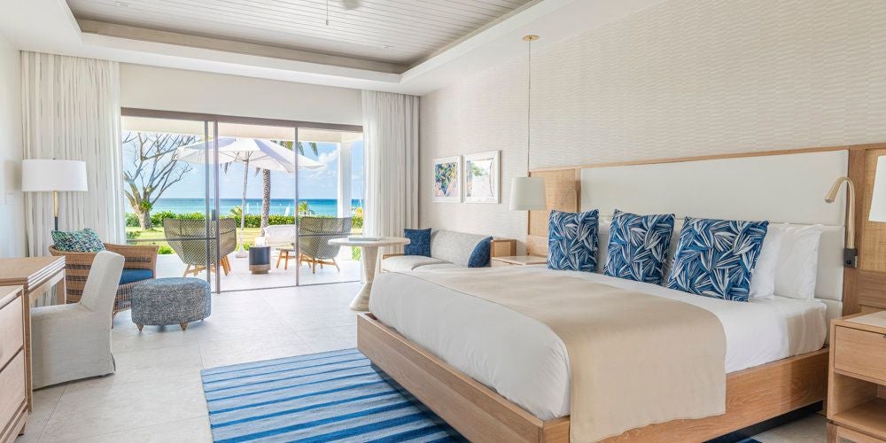 Luxurious Junior Suite with elegant four-poster bed, pristine white linens, and expansive ocean view from private balcony at Jumby Bay Island Resort, Antigua