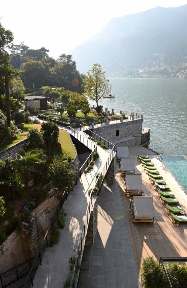 Modern luxury hotel with geometric wood facade perched on Lake Como's edge, surrounded by mountains and lush greenery