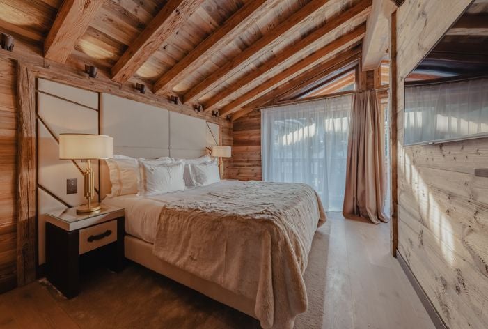 Luxurious alpine ski resort bedroom with plush white bedding, panoramic mountain views, and modern elegant wood-paneled design in Courchevel, France