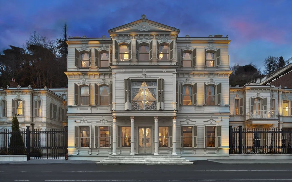 Luxurious Ottoman-style mansion in Istanbul, stone facade glowing at dusk with elegant windows and lush surrounding gardens.