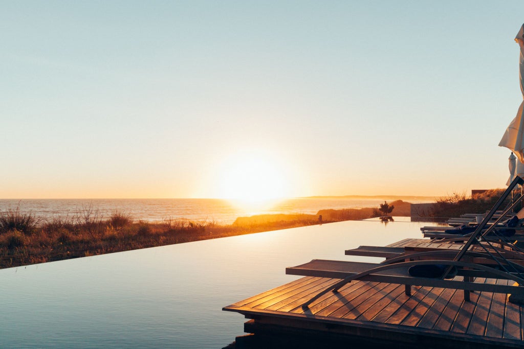 Luxurious modern beachfront hotel with glass walls, minimalist design, and sleek architecture overlooking golden sandy beach and turquoise ocean in José Ignacio, Uruguay