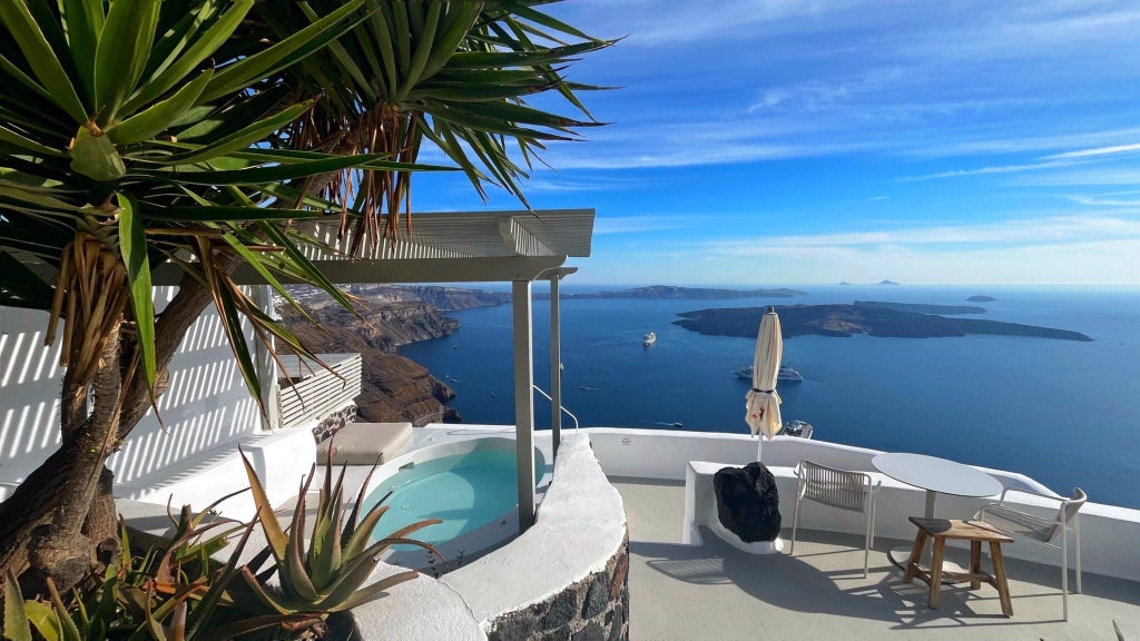 Luxurious Santorini cave suite with white-washed walls, panoramic caldera view, minimalist design, and elegant blue-trimmed private balcony overlooking Aegean Sea