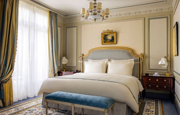 Opulent Parisian junior suite featuring gilded mirrors, crystal chandelier, Louis XV furniture, and silk damask walls in cream and gold tones