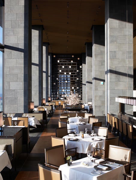 Japanese minimalist hotel lobby with towering stone walls, delicate paper lanterns, and a tranquil rock garden visible through floor-to-ceiling windows