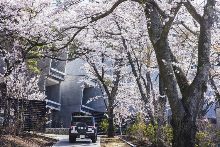 Modern luxury cabin with floor-to-ceiling windows perched on Mount Fuji hillside, overlooking Lake Kawaguchi and misty mountains at sunset