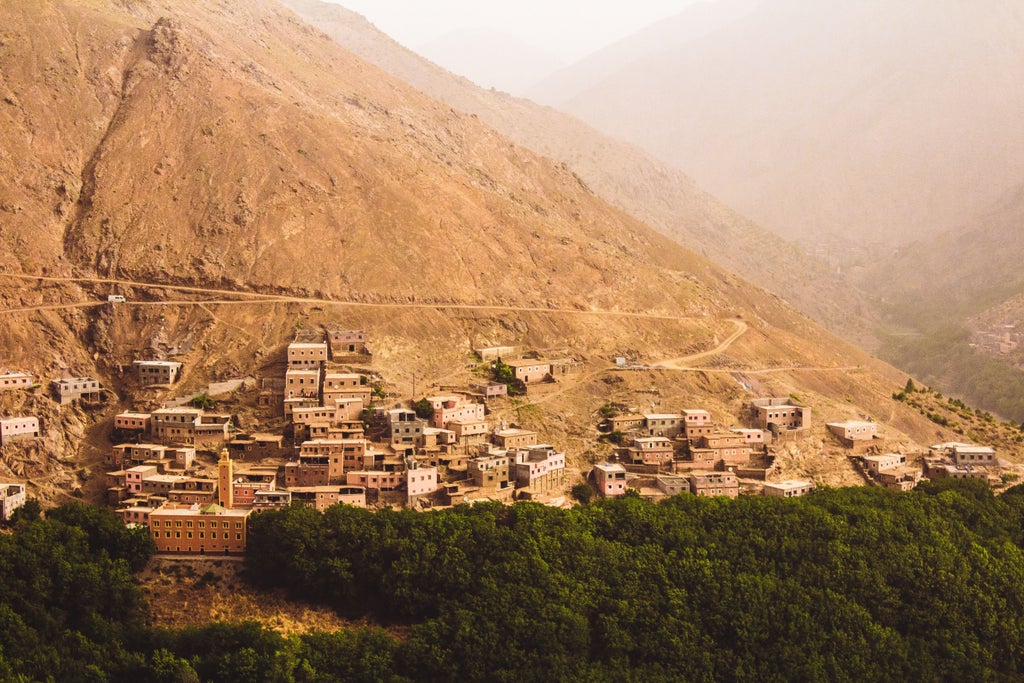 Snow-capped peaks of Morocco's High Atlas Mountains rise majestically against a clear blue sky, with rugged terrain and valleys below