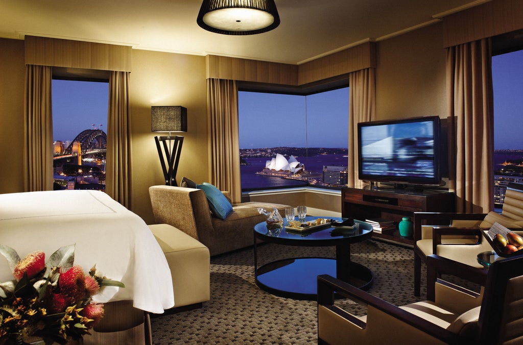 Contemporary hotel tower with reflective glass facade overlooking Sydney Harbour Bridge and Opera House at golden sunset