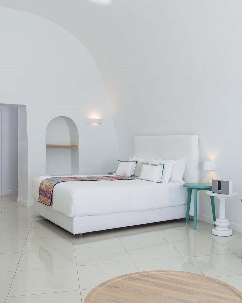 Luxurious white-walled honeymoon suite with jetted tub overlooking Aegean Sea, featuring minimalist Cycladic design in Santorini's iconic blue and white palette