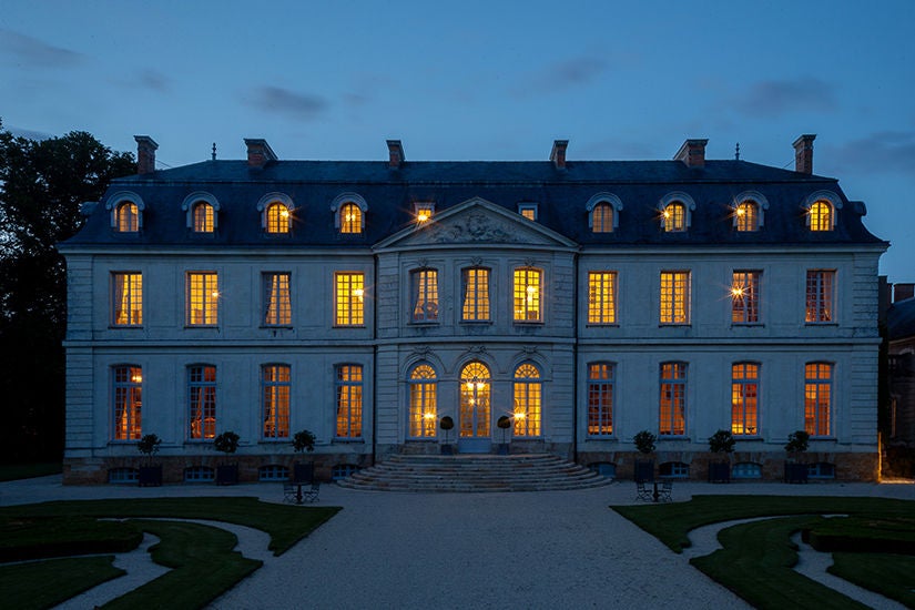 Majestic 18th-century French château hotel with limestone facade, ornate windows, and manicured gardens set against a blue summer sky