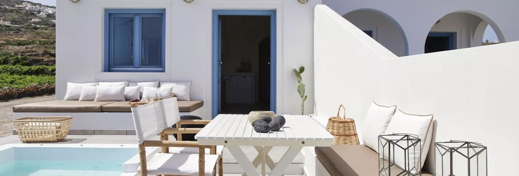 Luxurious white-walled Greek villa bedroom with minimal design, plush bed, natural wood accents, and panoramic view of scenic coastal landscape at sunset