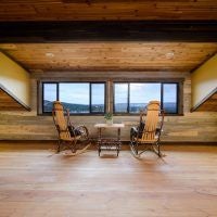 Rustic wooden lodge room with panoramic windows overlooking scenic mountain landscape, featuring plush king bed and warm earth-toned decor at Scenset Mountain Ranch