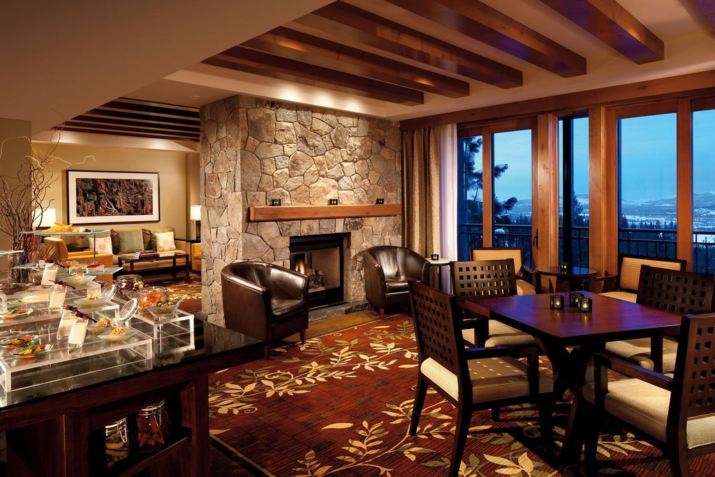 Luxury mountain lodge hotel with stone and wood facade, expansive windows, and snowy slopes of Lake Tahoe in background