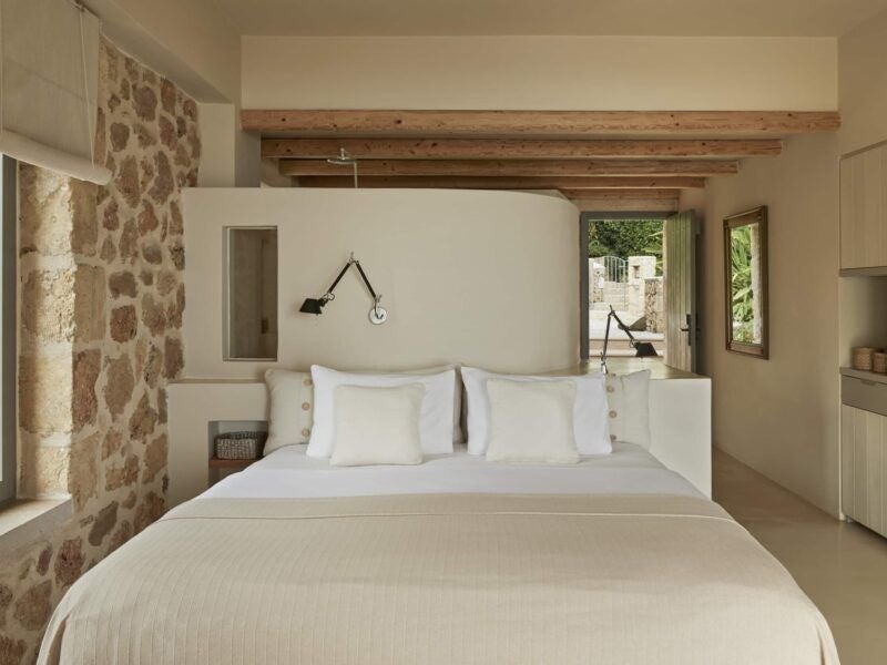 Elegant minimalist hotel room with white decor, wooden accents, and panoramic sea view overlooking Kefalonia's azure coastline and lush landscape