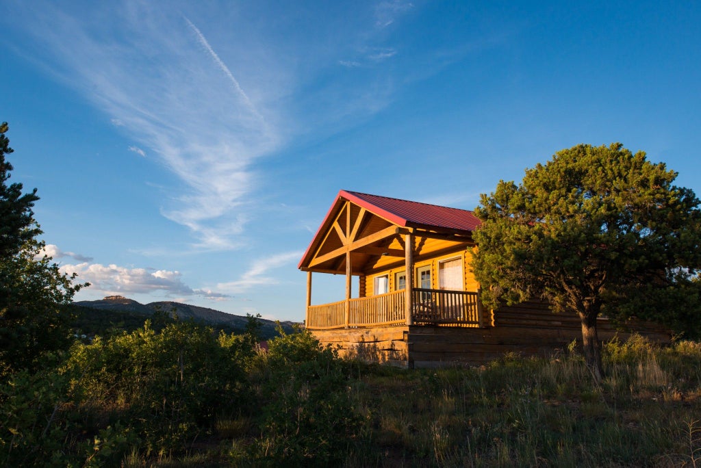 Rustic log cabin lodge nestled against scenic mountain backdrop, wooden deck with Adirondack chairs overlooking dramatic southwestern landscape near Zion National Park