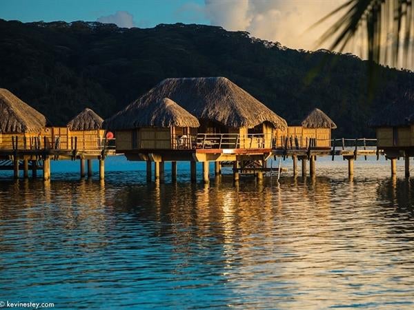 Luxurious overwater suite with private deck in Taha'a lagoon, featuring thatched roof, glass floor panels and turquoise ocean views