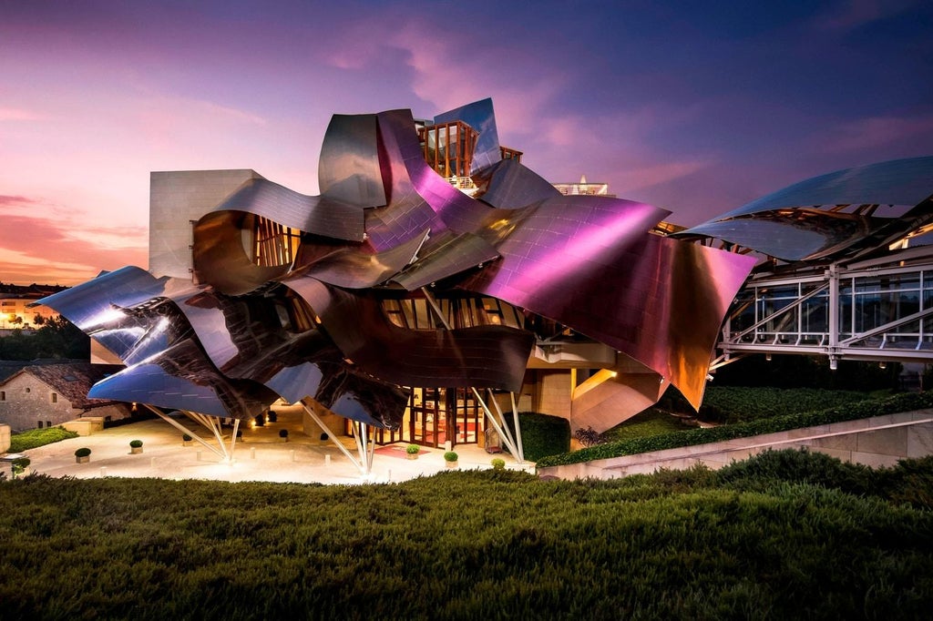 Luxurious Hotel Marqués de Riscal features dramatic curved titanium architecture in purple and silver, set against Spanish countryside hills