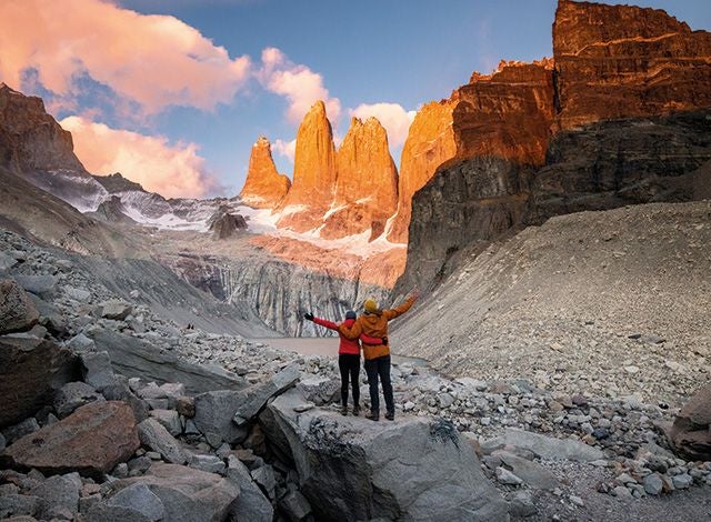 Rustic luxury hotel nestled in scenic Patagonian landscape with snow-capped mountains, wooden exterior, and lush green surroundings at golden hour