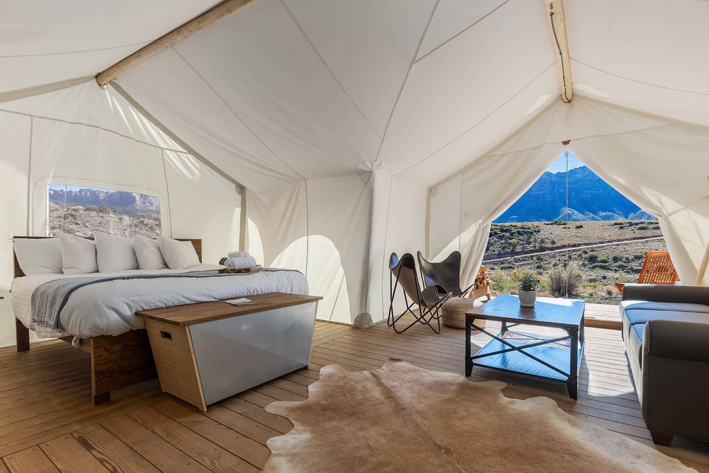 Luxurious safari-style canvas suite at Under Canvas Zion with king bed, rustic wood furnishings, and stunning desert landscape view through large tent window