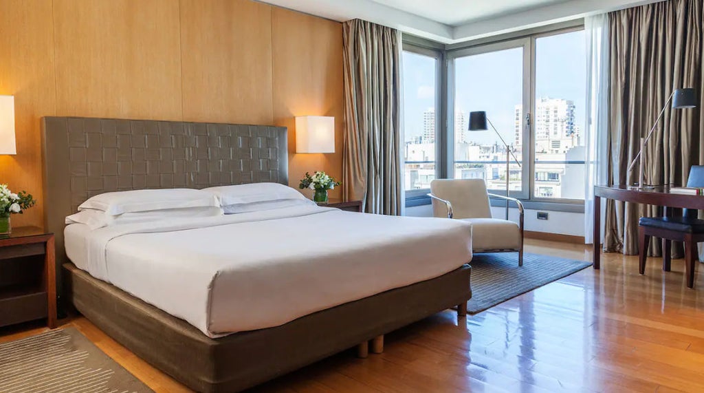 Elegant hotel room with king bed, crystal chandelier, marble bathroom entrance, and floor-to-ceiling windows overlooking Buenos Aires