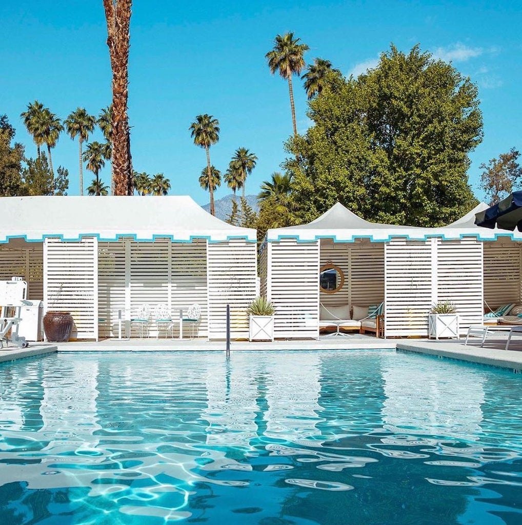 Elegant white luxury hotel with Spanish Colonial architecture, palm trees and manicured gardens set against Palm Springs mountains.