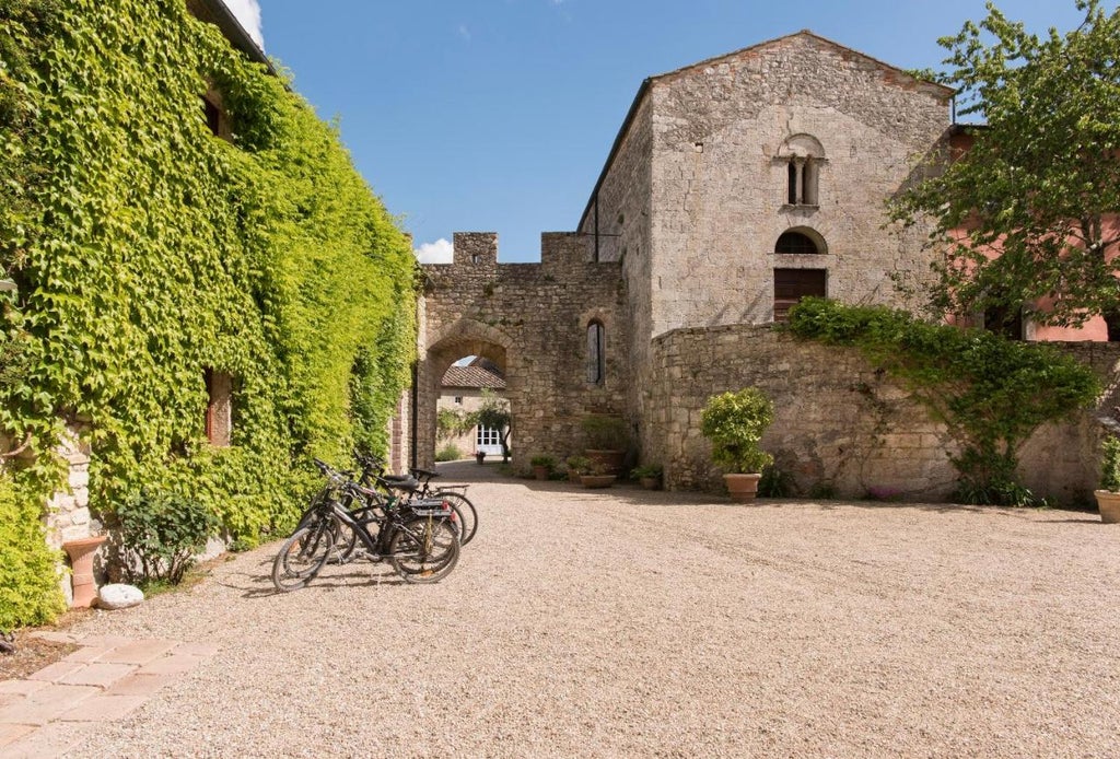 Historic Tuscan villa with stone facade set on hilltop, featuring manicured gardens, infinity pool overlooking rolling countryside at sunset