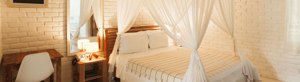 Elegant Brazilian hotel suite with wooden accents, featuring plush white bedding, minimalist decor, and warm tropical lighting in Trancoso