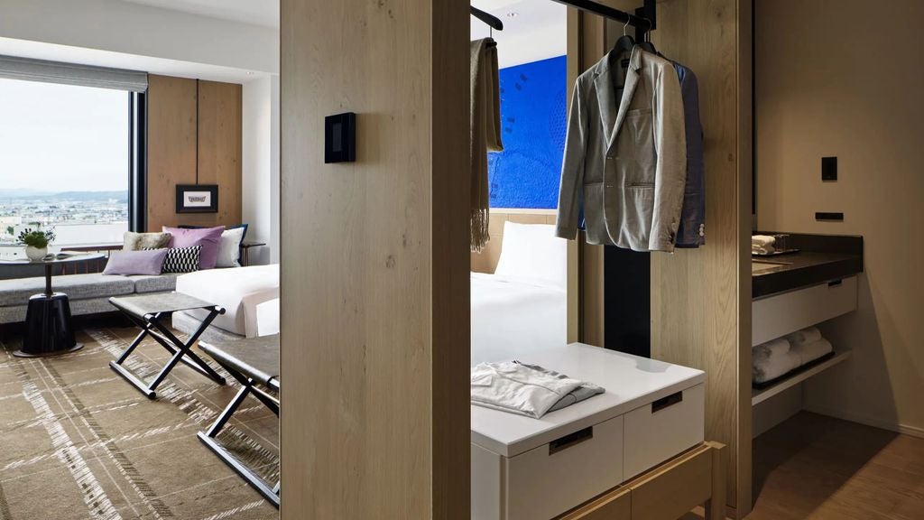 Modern twin hotel room with floor-to-ceiling windows, city views, plush white beds, wood accents and stylish seating area