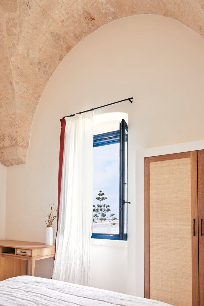 Rustic stone tower suite at Masseria Calderisi with elegant white linens, antique furnishings, and panoramic Puglian countryside views through arched windows