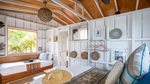 Elegant Argentine hotel room with plush white bedding, blue coastal accents, wooden furnishings, and soft natural light highlighting Coral Caye's serene beachside aesthetic