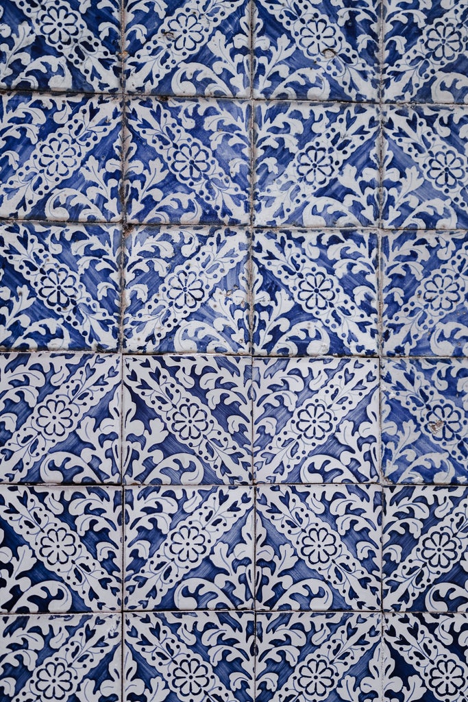 Intricate blue and white azulejo tiles hand-painted during artisan workshop, showcasing traditional Portuguese craftsmanship in sun-drenched ceramic studio