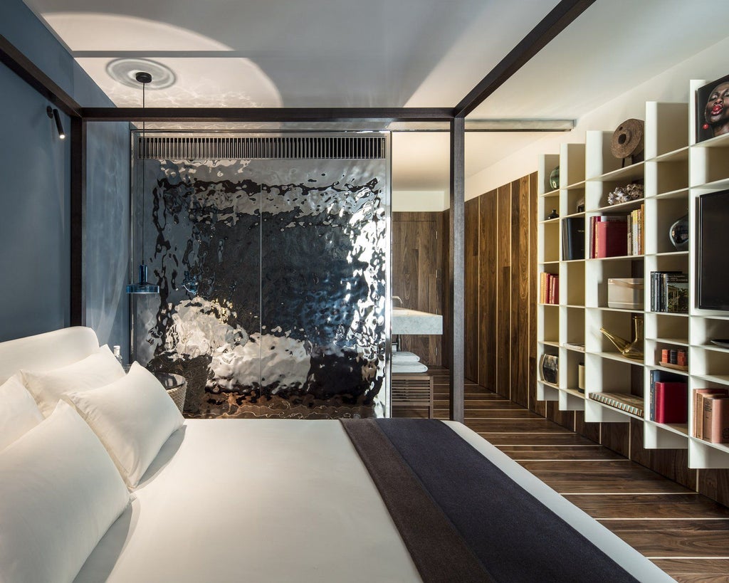 Minimalist white bedroom with wood accents, sleek design, and floor-to-ceiling windows overlooking a vibrant Spanish coastal landscape at Sir Joan Hotel.