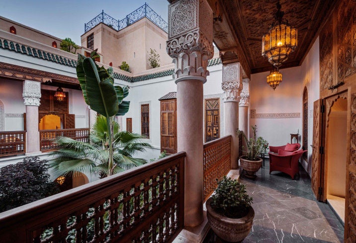 Elegant Moroccan riad courtyard with ornate archways, traditional lanterns, and plush seating around a central fountain with lush plants