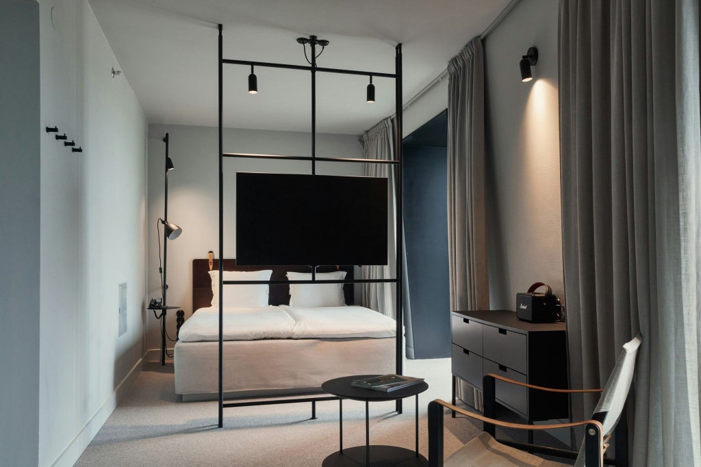 Modern Nordic hotel studio with minimalist design, sleek grey furnishings, floor-to-ceiling windows revealing urban Stockholm skyline at sunset