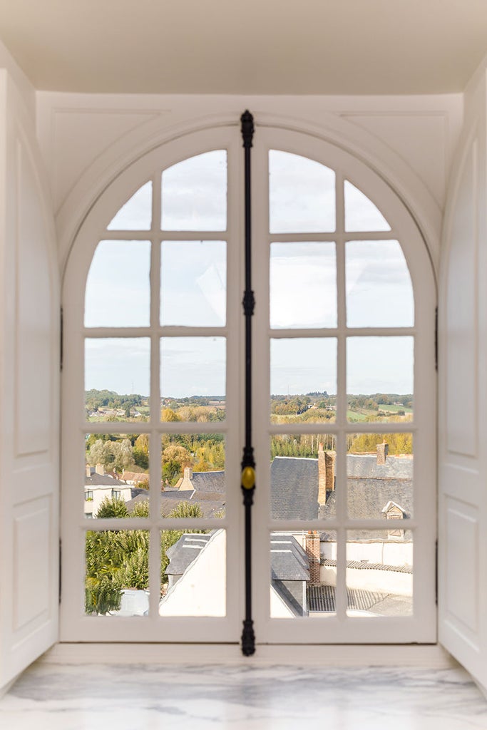 Elegant corner suite with high ceilings, ornate crown molding, crystal chandelier, and panoramic Loire Valley views through floor-to-ceiling windows