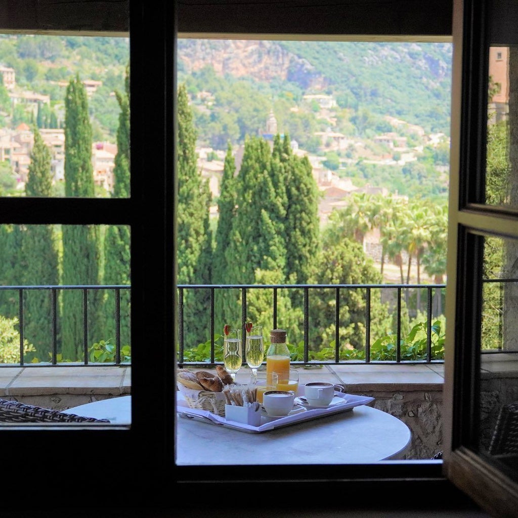 Elegant stone manor hotel nestled in Mallorca's mountains, featuring manicured gardens, terracotta roofs and panoramic valley views