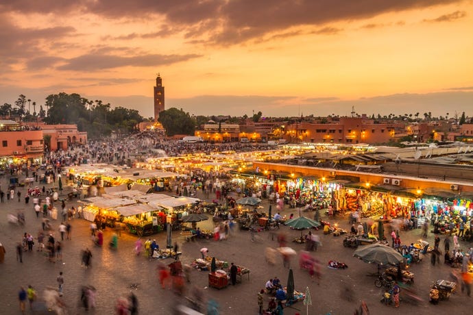 A classic view of Jemaa El Fna square in Marrakech at sunset with musicians, acrobats, storytellers, food stalls, and markets buzzing into the night