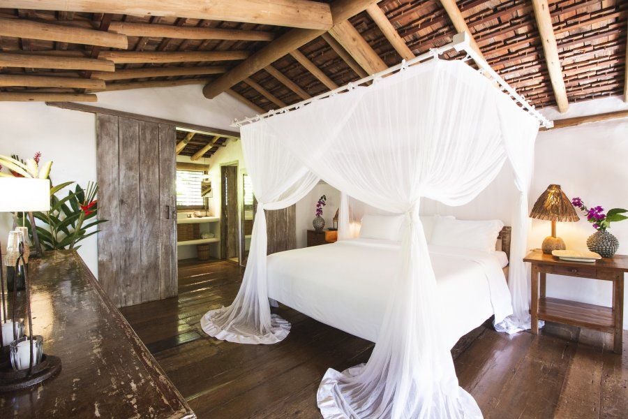 Luxurious Brazilian eco-resort bedroom with rustic wooden furnishings, warm earth tones, and traditional local design elements in Trancoso, Bahia